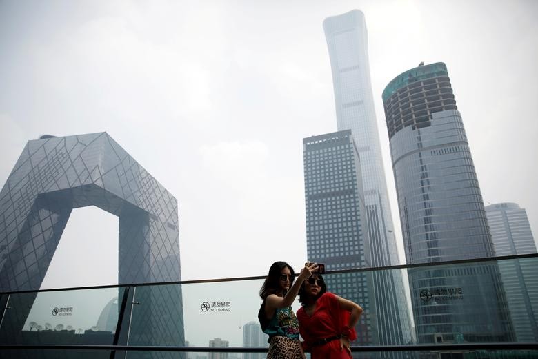 Women pose for pictures at a shopping mall near the CCTV headquarters and China Zun skyscraper in Beijing's central business district (CBD), China. REUTERS/Tingshu Wang    